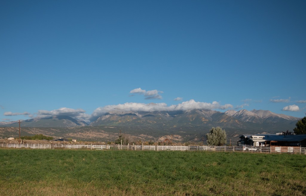 Ute Range of mountains in the distance, their tops hidden by clouds. Mid distance low moraine hills; foreground green pasture.